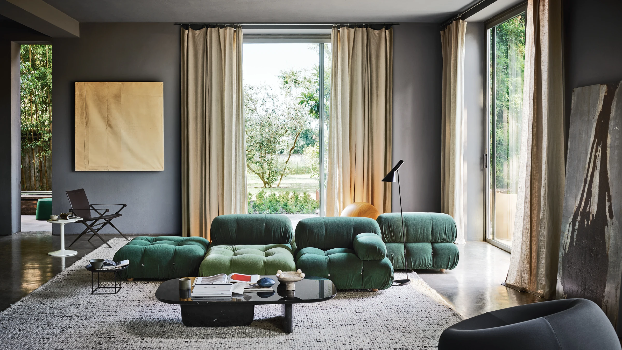 Green B&B Italia Camaleonda modular sofa beside tall curtained windows overlooking a garden