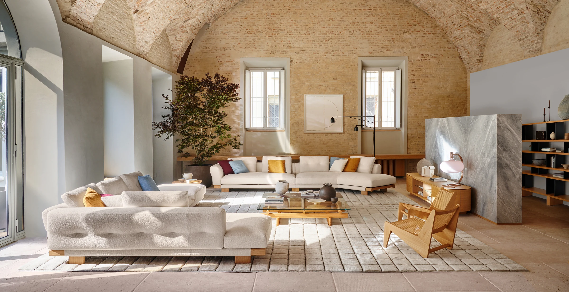 Cream Cassina Sengu sofas and warm wood furniture beneath a vaulted stone ceiling